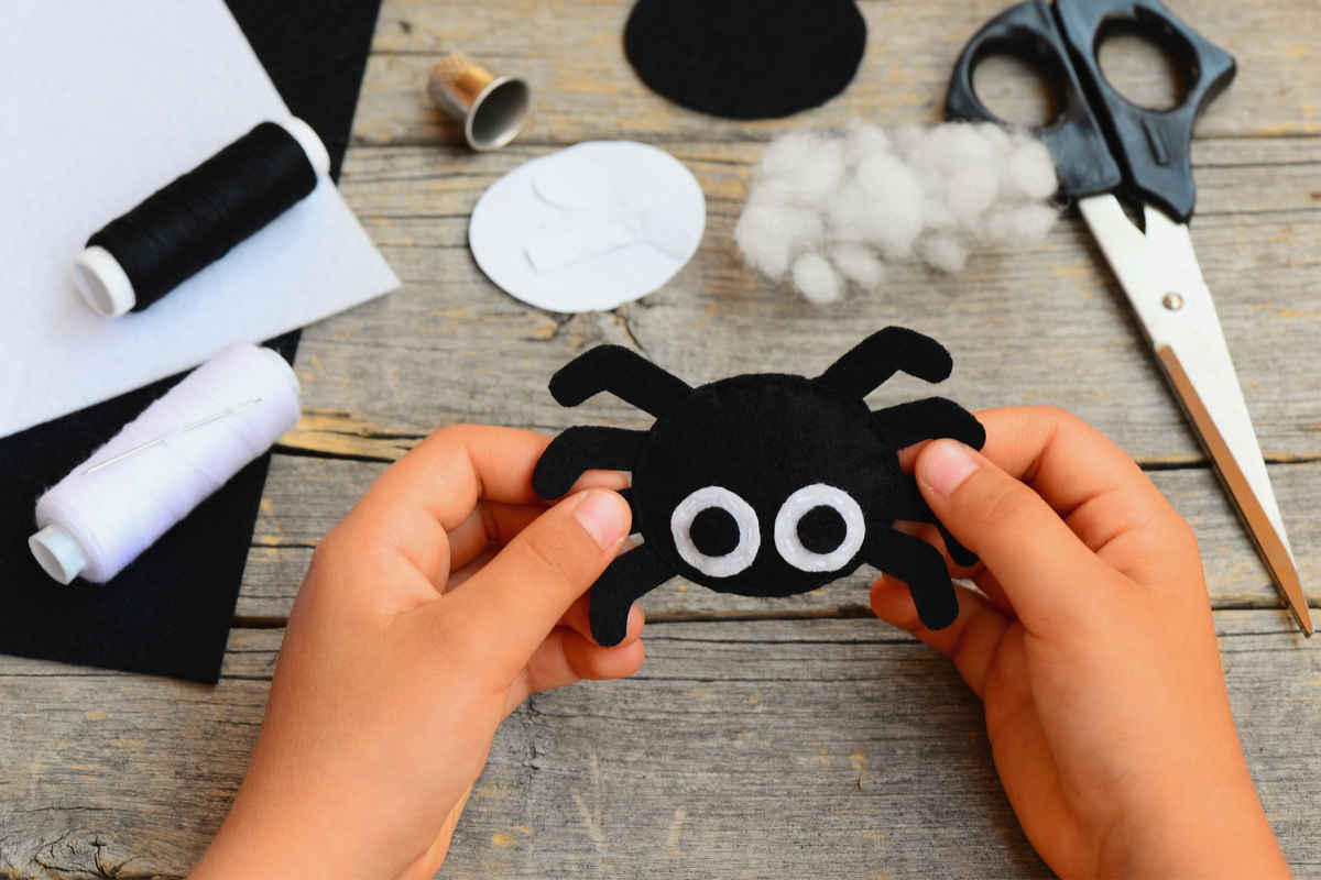 materiali vari per creare decorazioni fai da te per halloween come filo bianco e nero, forbici e mani di un bambino che tengono un ragno di carta