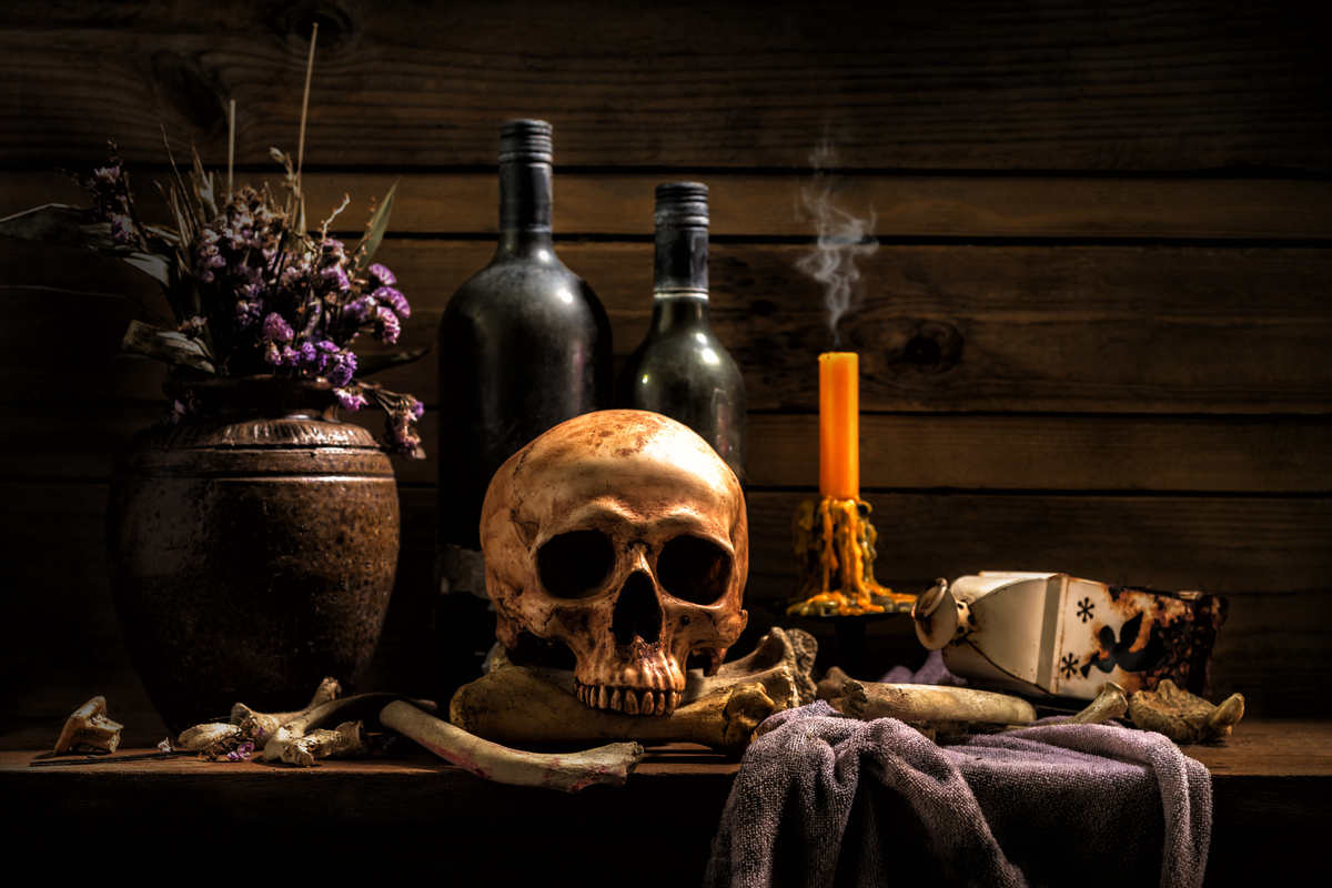 Teschio, ossa, bottiglie di vino, lume di candela, su vecchio tavolo in legno e vaso con fiori di colore viola 