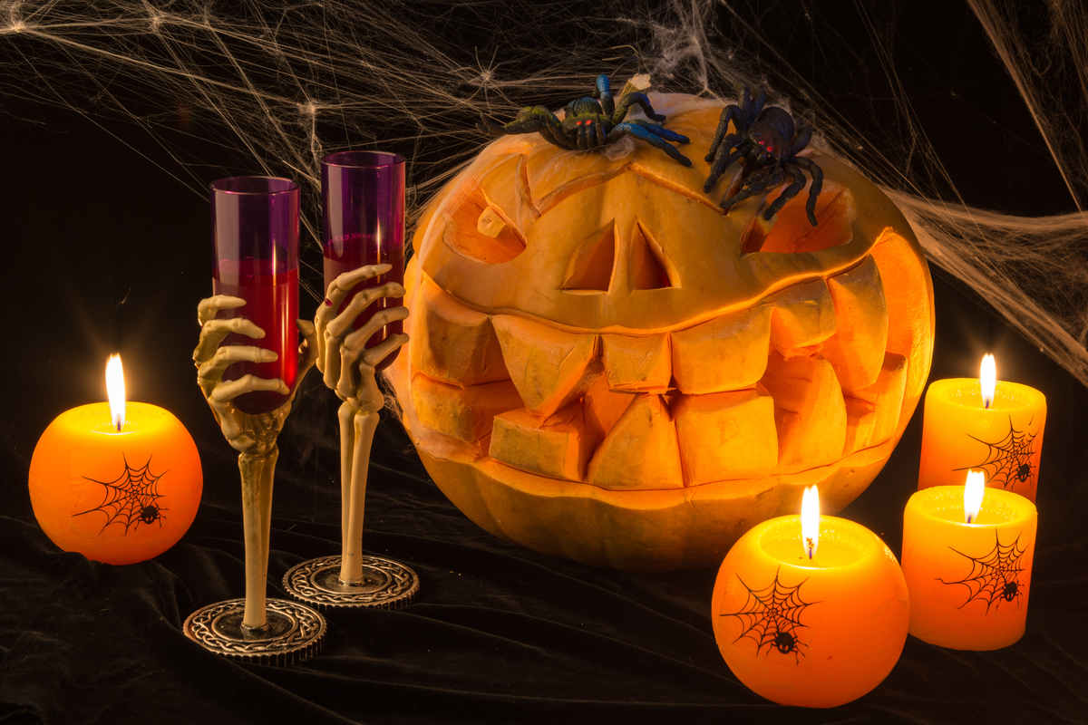 zucca intagliata per halloween con ragni e ragnatele, candele accese e due calici bicchieri con stelo a forma di mano