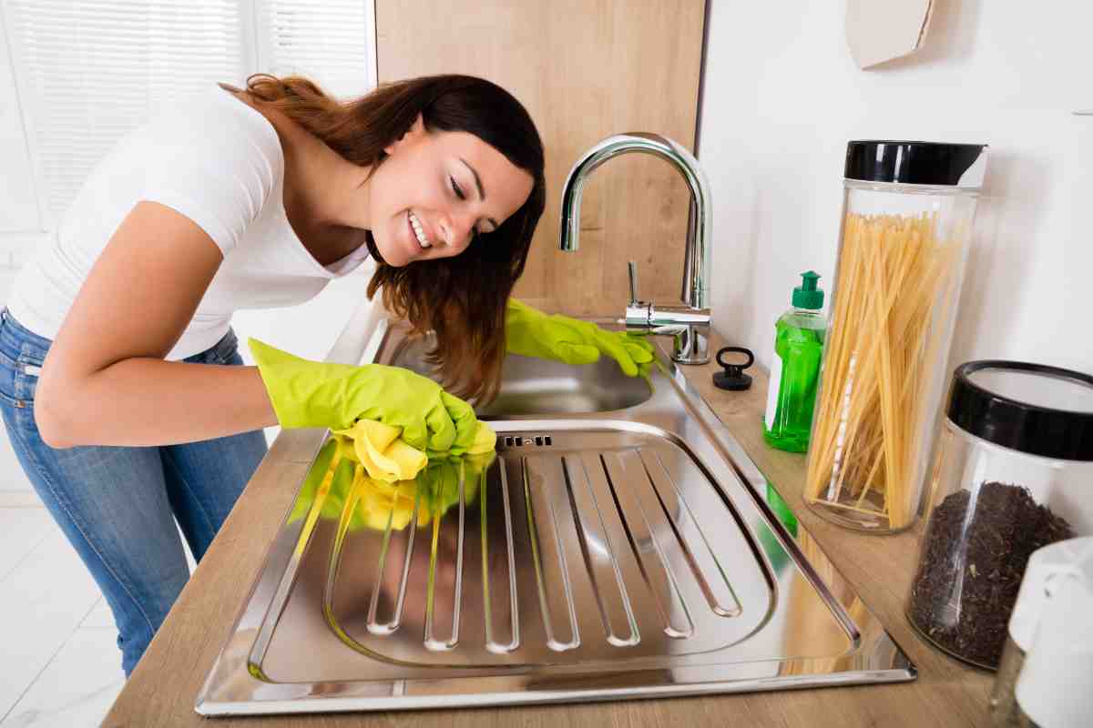 donna pulisce il lavello in acciaio della cucina