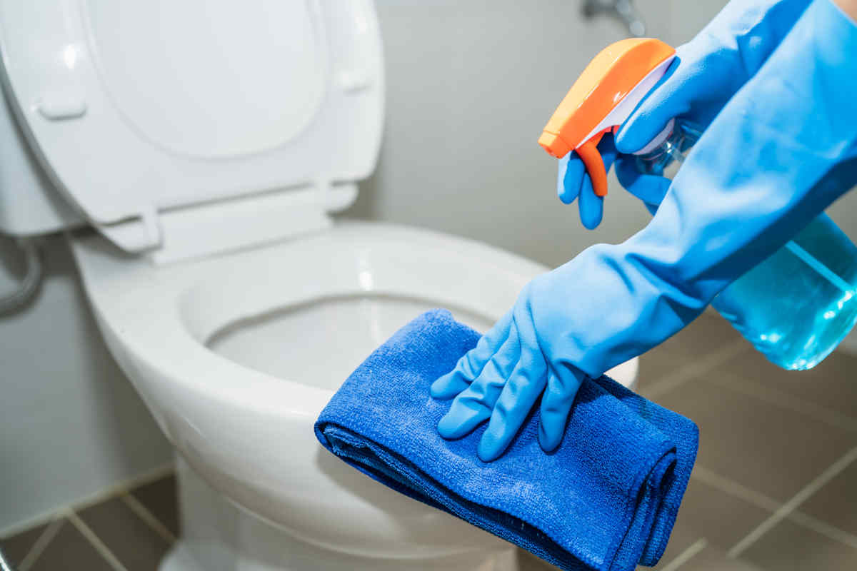 persona pulisce i sanitari con guanti e spugna