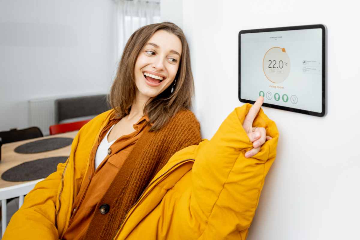 ragazza sorridente con il dito sul panello del termostato ambiente