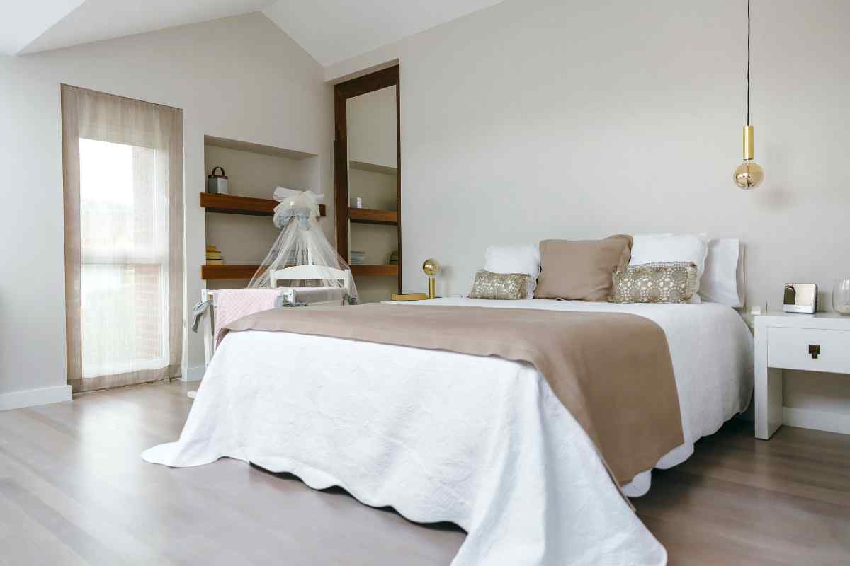 Letto con biancheria di colore bianco e parquet sul pavimento