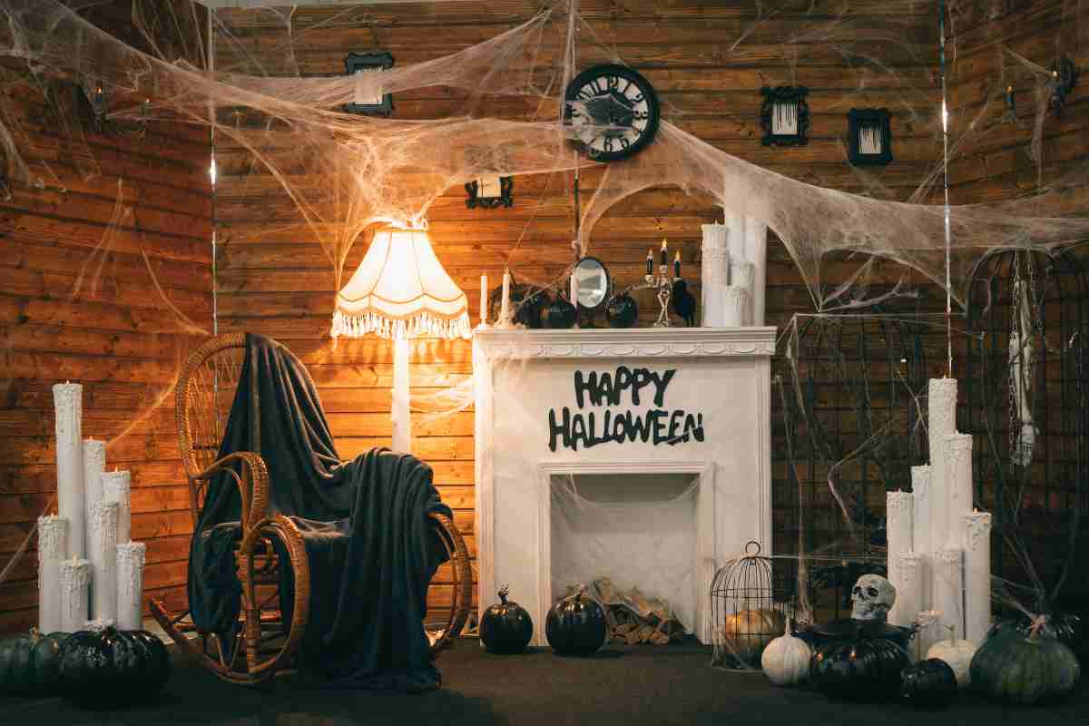 camino con scritta happy hallowen, ragnatele sulla parete, ceri e lanterne, zucche bianche e lampada illuminata