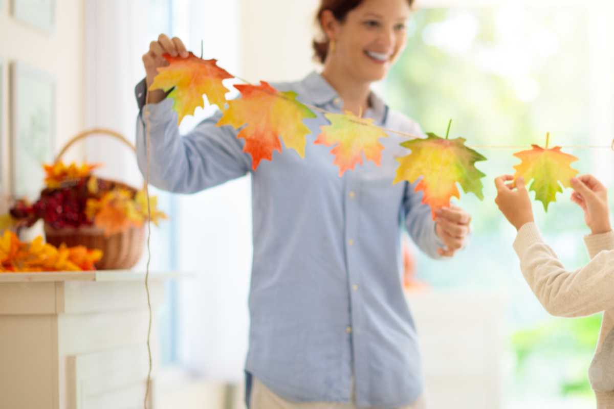 mamma e bambino appendono la decorazione autunnale di foglie alla finestra
