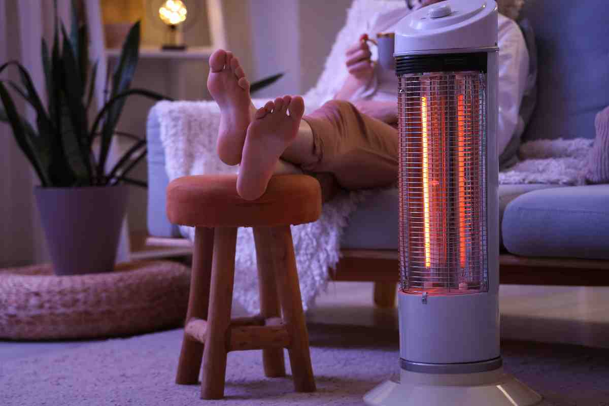 persona sul divano con i piedi sullo sgabello vicino a una stufa elettrica