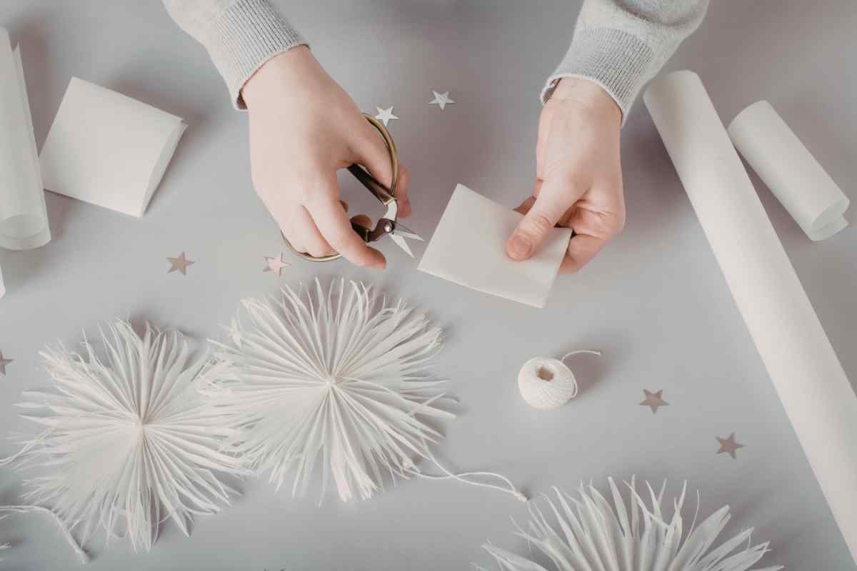 mani che realizzano decorazioni natalizie fai da te in carta e filo