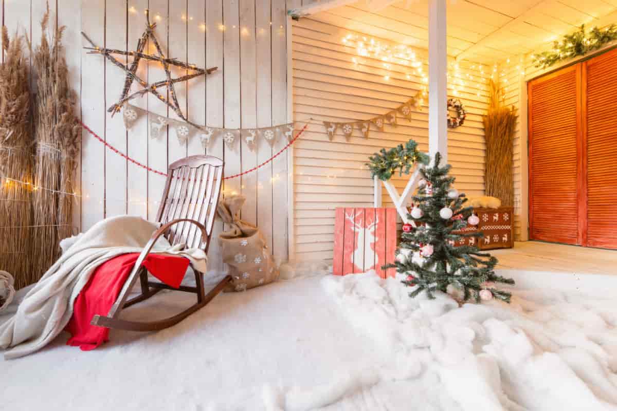 balcone decorato con neve finta, sedia a dondolo, albero di natale, lucine e decorazioni a forma di stella appesa sulla parete