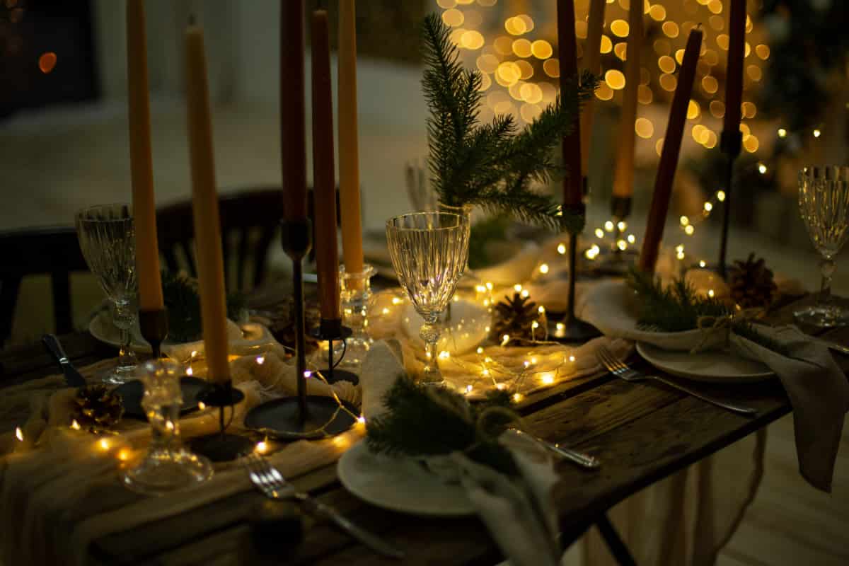 tavola allestita e apparecchiata con decorazioni natalizie, candele e luci calde