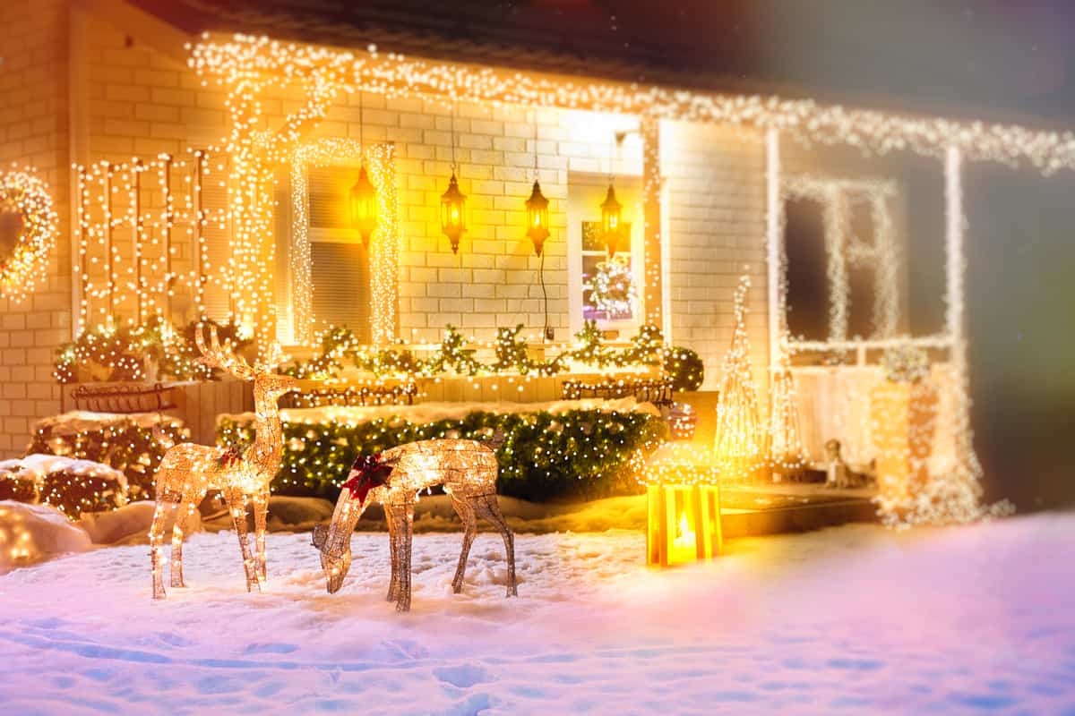 giardino innevato con casa sullo sfondo con luci natalizie e due renne finte illuminate sul giardino