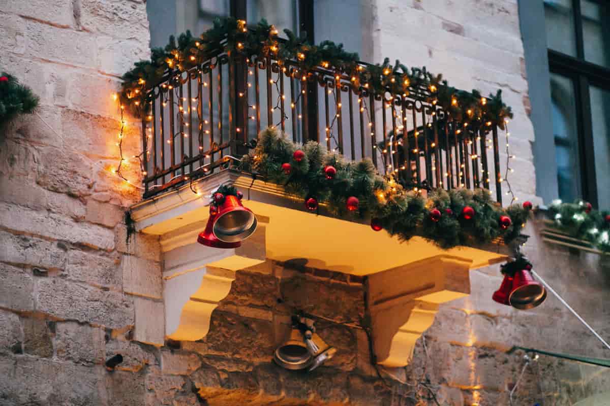 festoni di colore verde appese sulla ringhiera di un balcone con lucine natalizie e campanelline rosse