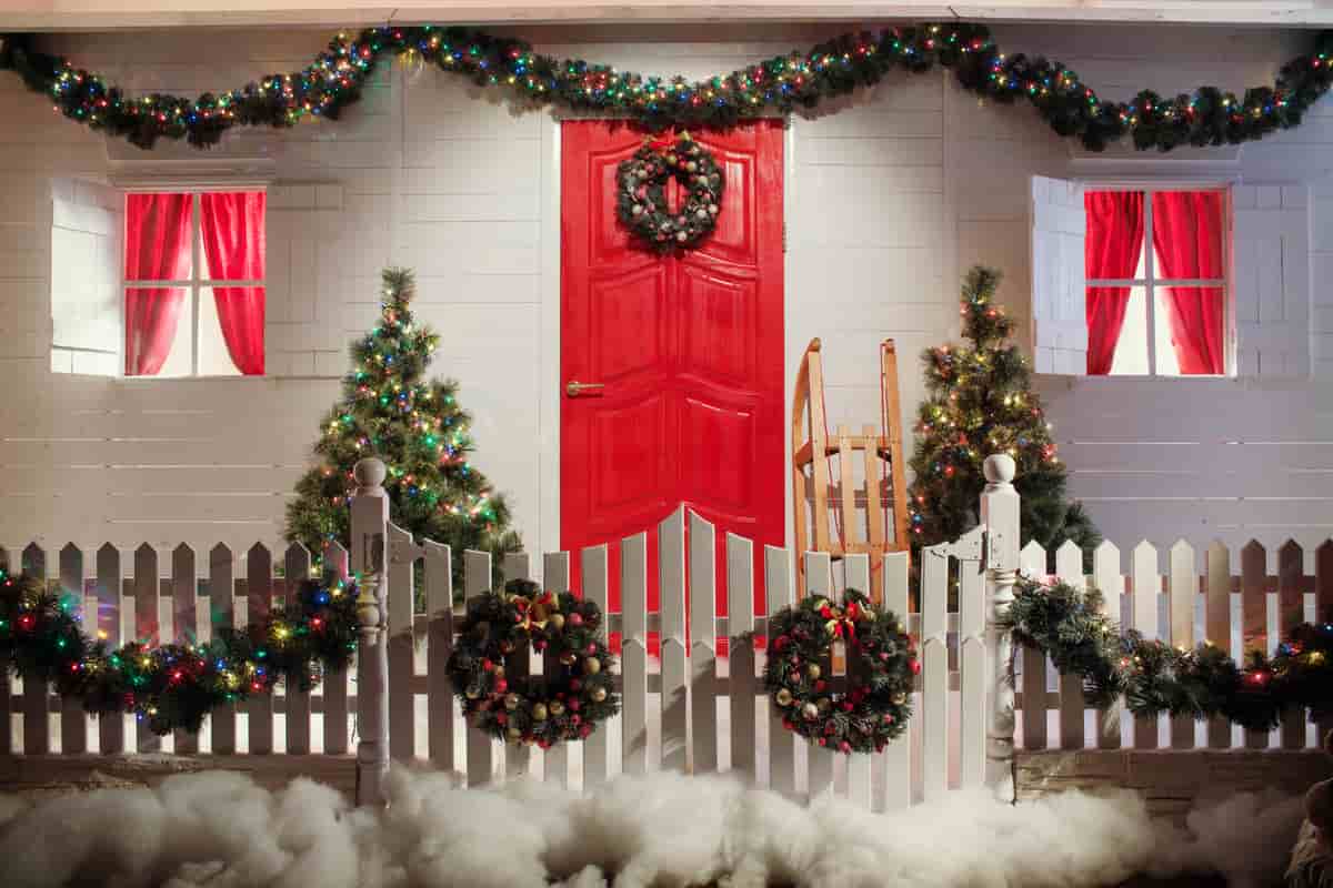 esterno di una casa con staccionata bianca e porta di colore rosso, con ghirlande di colore verde e festoni come decorazioni natalizie