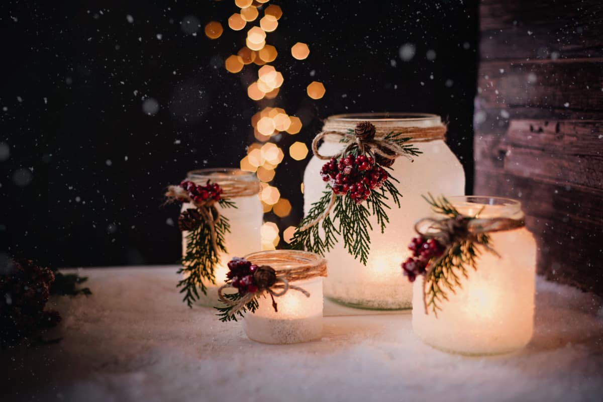 barattoli decorati di bianco e con ramoscelli di pino per Natale con candele poggiati su neve bianca
