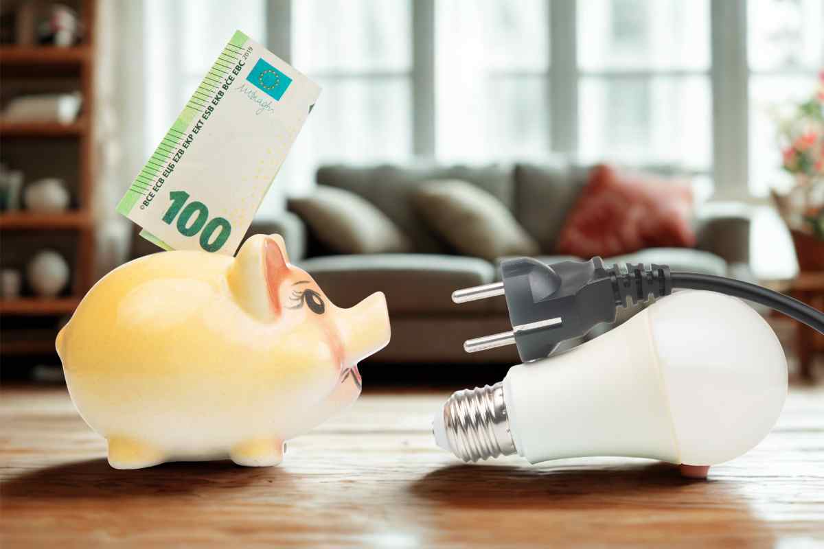 lampadina led e presa vicino a salvadanaio con 100 euro