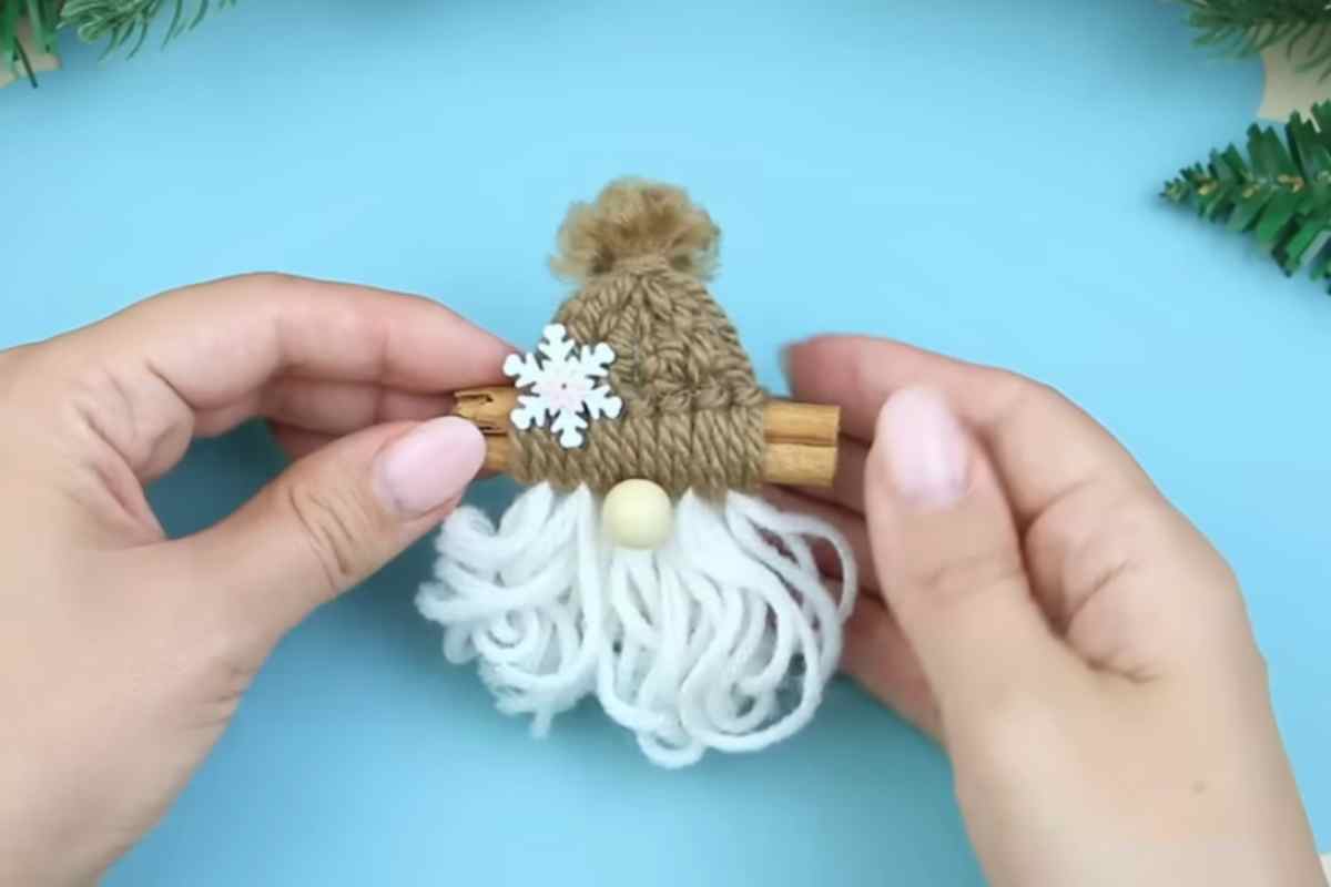 Gnomo di Natale di lana con stecca di cannella tra due mani