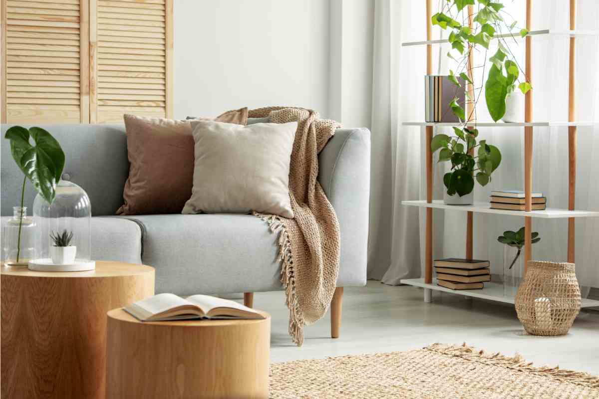 ambiente living con materiali naturali, tavolini in legno, divano e tessili in fibra grezza e libreria con piante