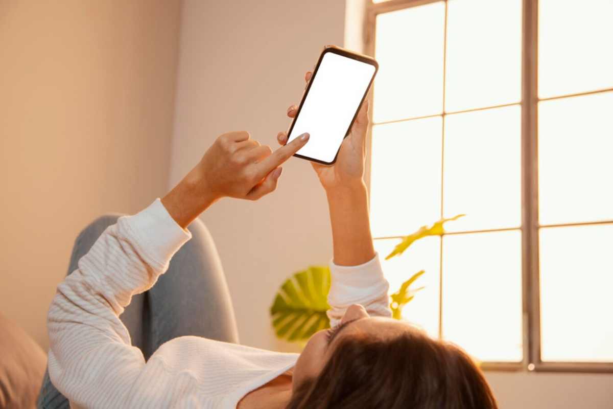 ragazza sdraiata sul letto controlla le tapparelle con il telefono