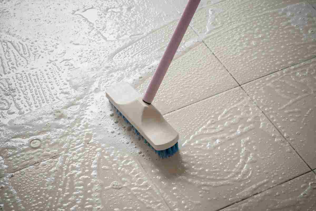 persona effettua pulizia con spazzola e detergente su pavimento