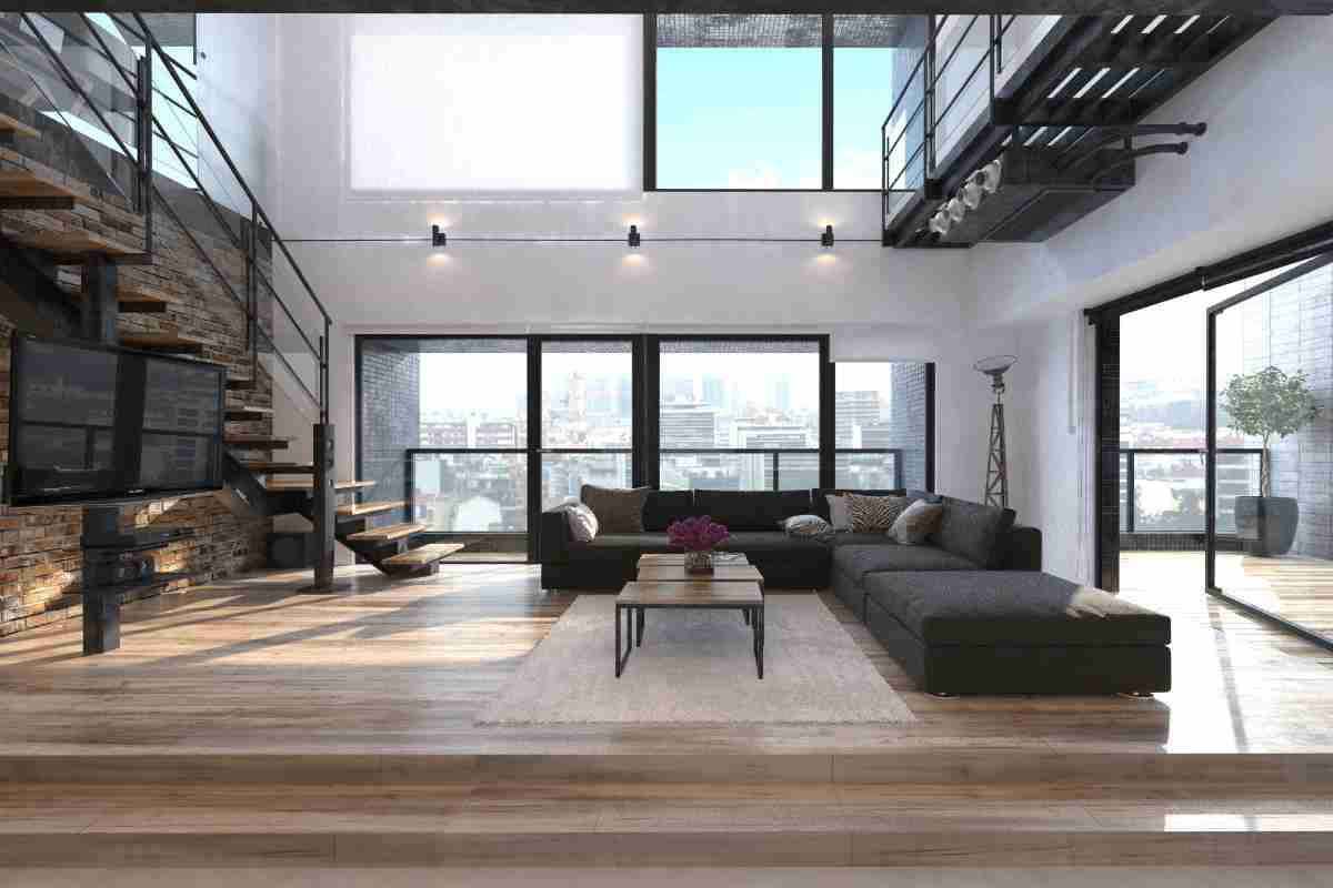 ampia sala open space con parquet in legno e divano nero con scale con struttura in metallo nero e gradini in legno