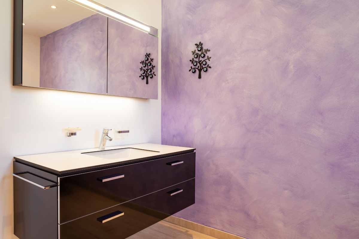 Bagno con parete lilla e mobile lavabo nero con piano bianco