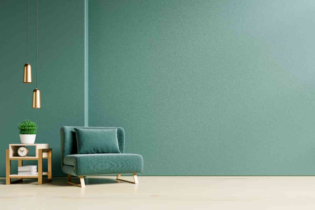 parete verde salvia con davanti una poltrona letto stile con cuscino della stessa tonalità e un tavolino con lampade sospese in metallo