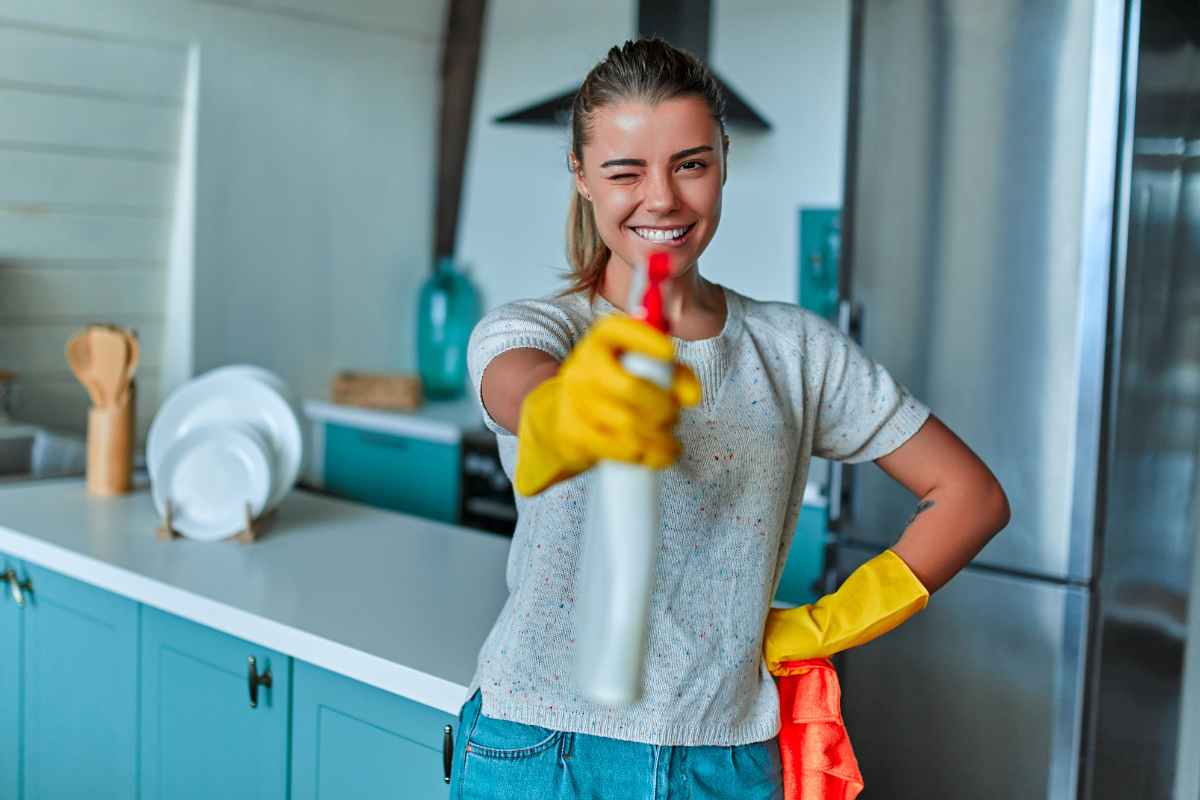ragazza sorridente che fa l'occhiolino puntando il flacone spray con lo sgrassatore fai da te