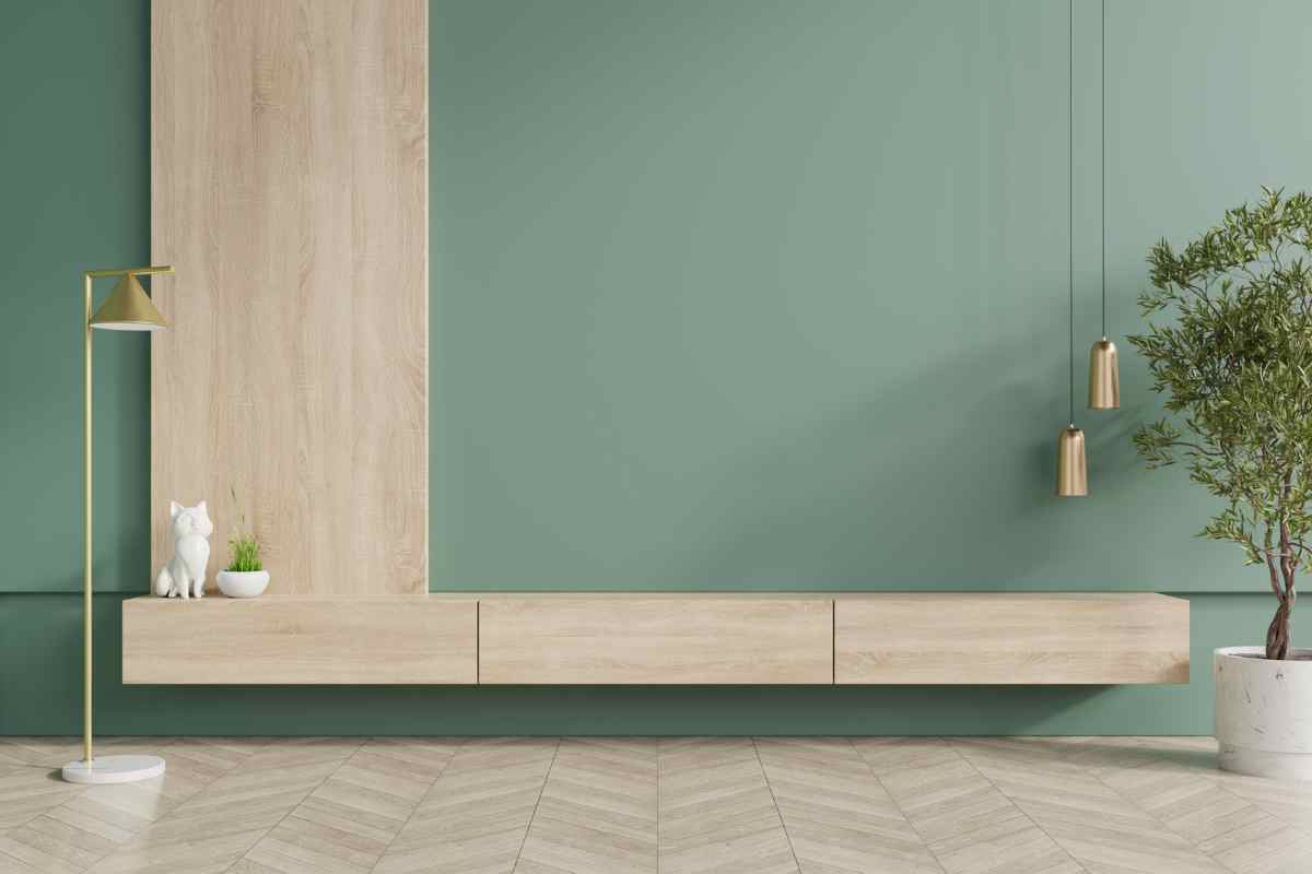 soggiorno con parete verde salvia attrezzata con mobili sospesi in legno chiaro