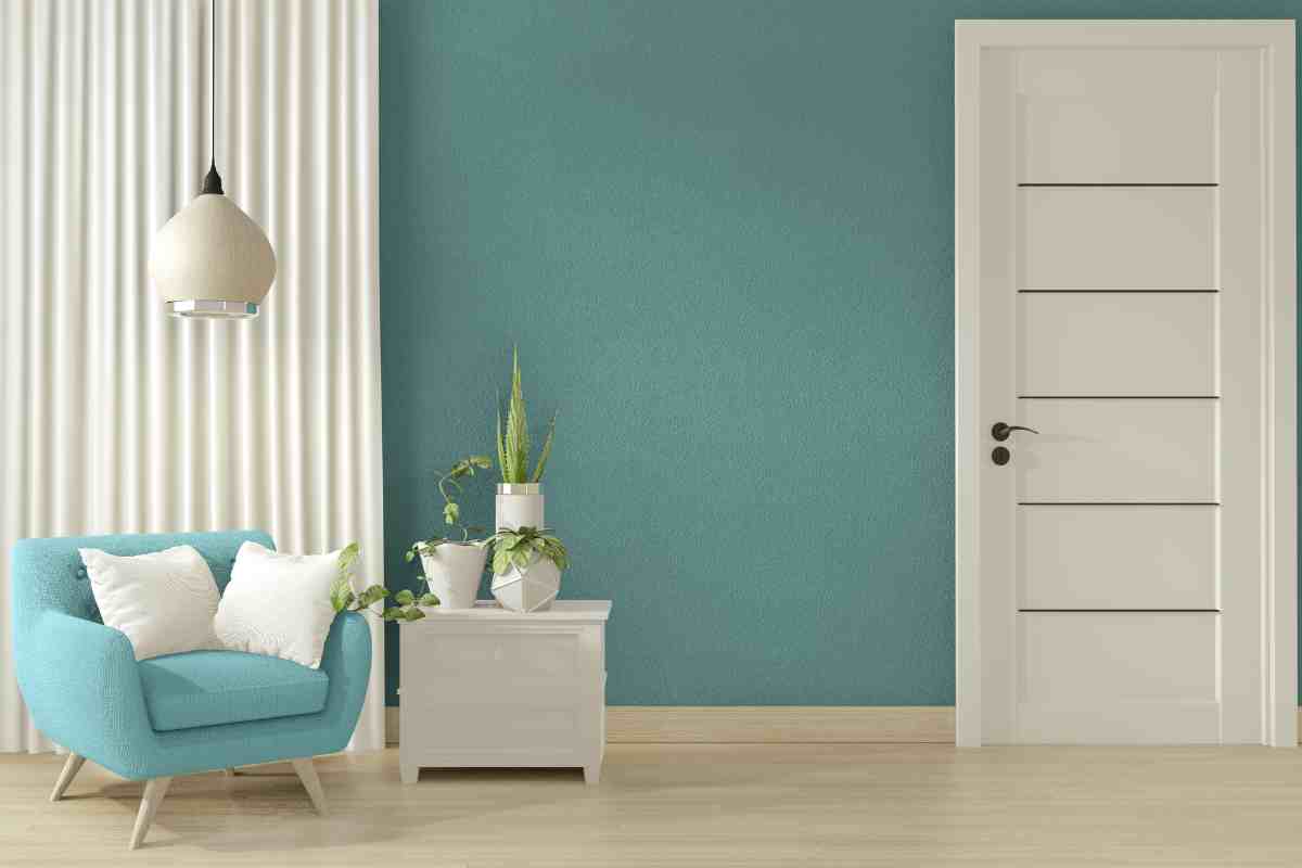 Parete di un soggiorno color ciano con davanti una poltrona della stessa tinta con arredi bianchi