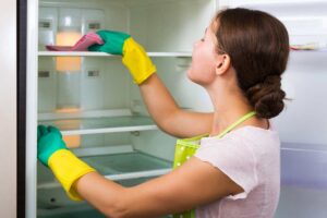 Frigorifero aperto e donna intenta nelle pulizie