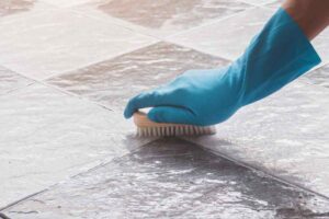 mano con guanto e spazzola pulisce le fughe tra le piastrelle in terrazzo