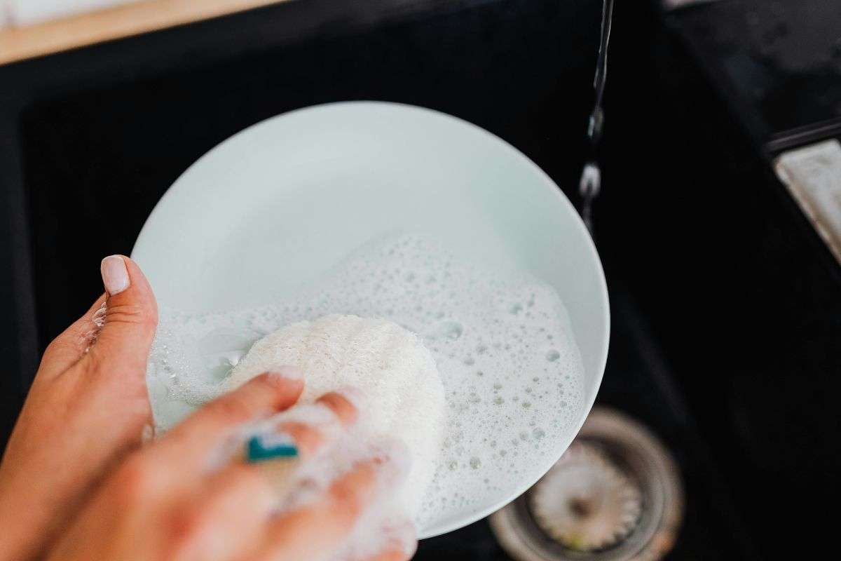 Mano che lava piattino da caffè con sapone