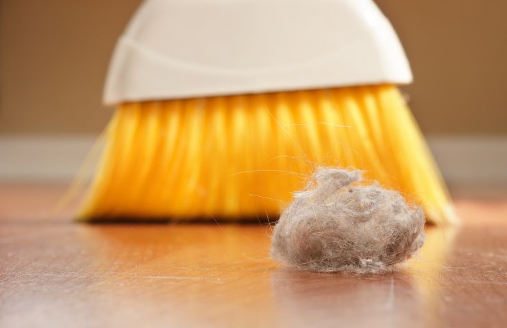 scopa che rimuove accumulo di polvere dal pavimento