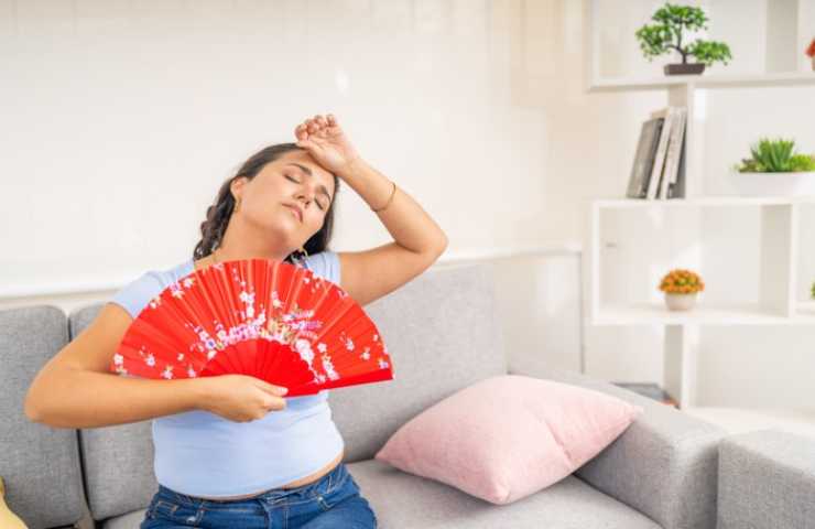 Donna con ventaglio che sente caldo seduta su divano grigio