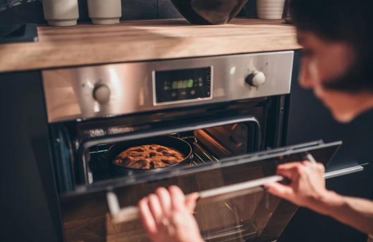 donna che apre il forno con dentro una torta 