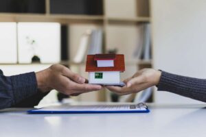 Mani che si scambiano il modellino di una casa