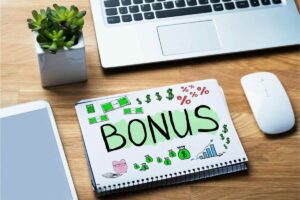 Quaderno con scritto bonus, disegno banconote, dollaro, percentuale, grafico, e PC