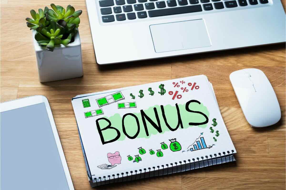 Quaderno con scritto bonus, disegno banconote, dollaro, percentuale, grafico, e PC