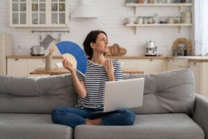 Donna sul divano con ventaglio e PC, soffre il caldo