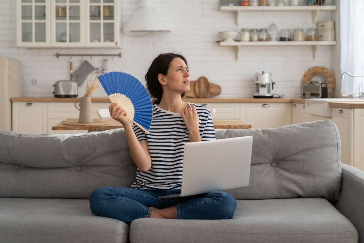 Donna sul divano con ventaglio e PC, soffre il caldo