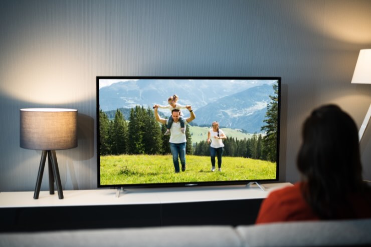 donna sul divano che guarda famiglia in montagna in tv