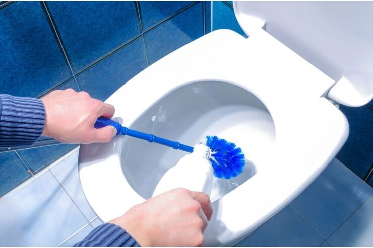 Mano che versa prodotto nello scarico del WC e usa scopino blu