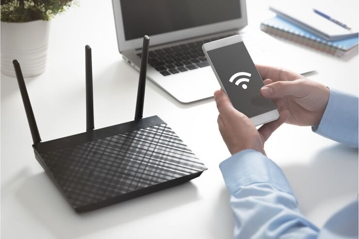 Uomo tiene in mano cellulare con segnale Wifi sullo sfondo, modem e PC