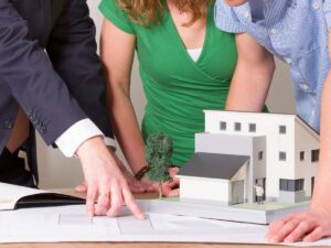 persone guardano piantina abitazione e casa in miniatura
