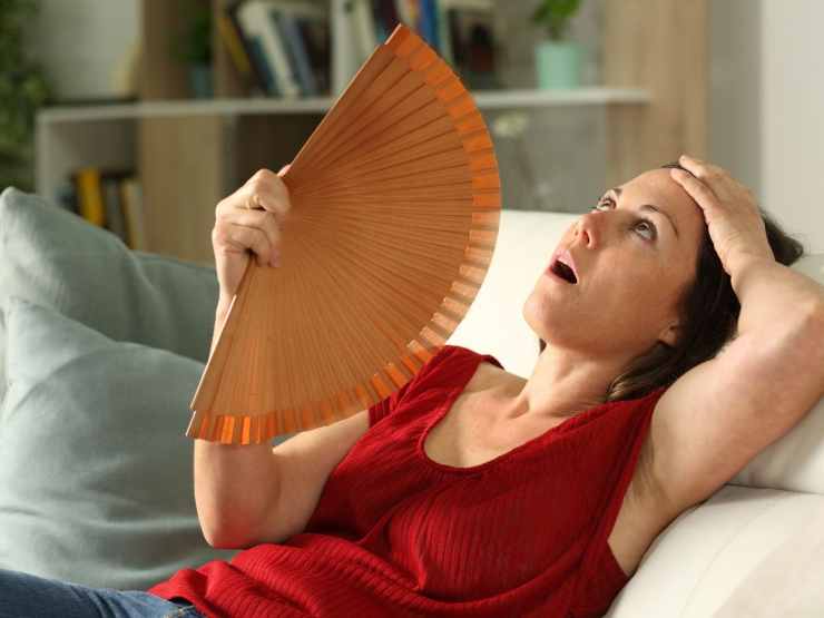 Donna disperata sul divano che utilizza ventaglio