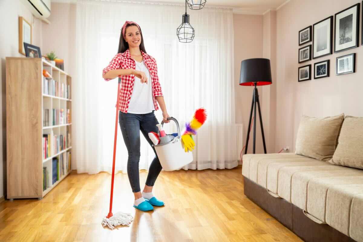 Ragazza con spazzolone, secchio e strumenti per fare le pulizie, sorridente