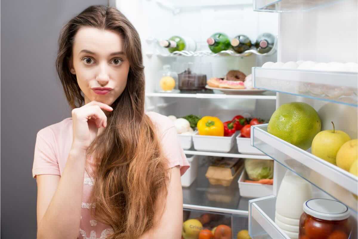 Donna pensierosa davanti al frigorifero aperto