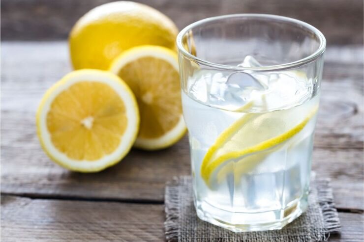 Bicchiere con acqua e ghiaccio e fette di limone, limoni