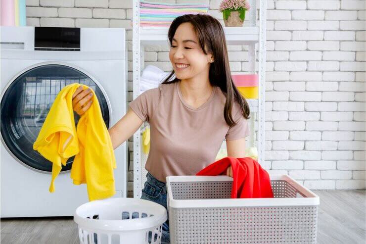 Donna smista capi di abbigliamento nelle ceste, dietro di lei lavatrice