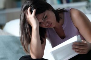 Ragazza legge documento tenendosi la mano nei capelli, affranta