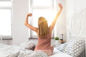 Donna seduta sul letto al mattino si sgranchisce le braccia